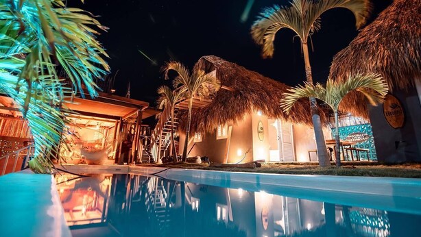 A resort with a pool, thatched-roof buildings, and palm trees at night. - Kokohau Bungalows - Adults Only (Juan de Acosta)