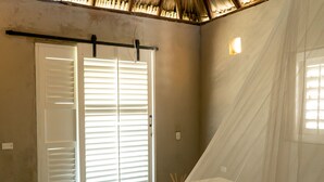 A room with a bed, a window with blinds, a door, and a ceiling with a thatched roof. - Kokohau Bungalows - Adults Only (Juan de Acosta)