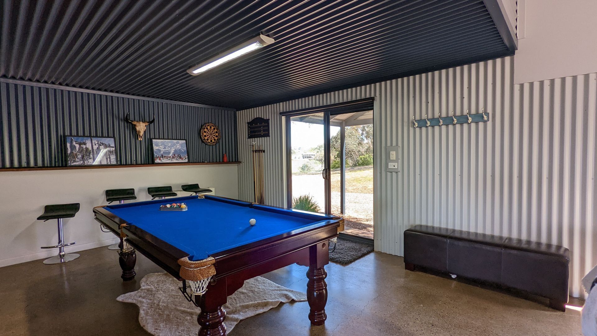 Una mesa de billar con superficie de fieltro azul, un dardo y una decoración de toro en la pared.