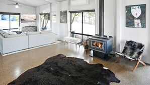 Un salon moderne avec un canapé, un banc blanc, un grand tapis noir, une cheminée et un fauteuil recouvert de fourrure.