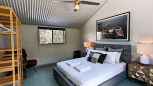 Une chambre à coucher avec un lit, deux lampes de chevet, un ventilateur de plafond, une fenêtre et un tableau encadré au mur.