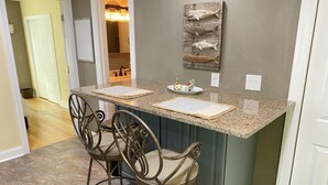 Una cocina con encimera de granito, dos taburetes de bar y un adorno en la pared.
