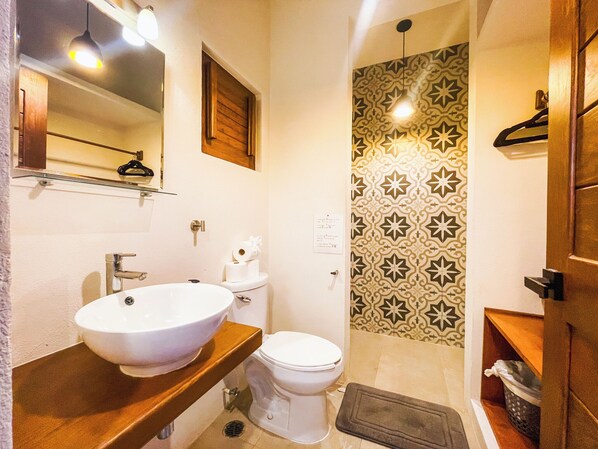 A bathroom with a wooden vanity, a white sink, a toilet, and a shower area with patterned tiles.