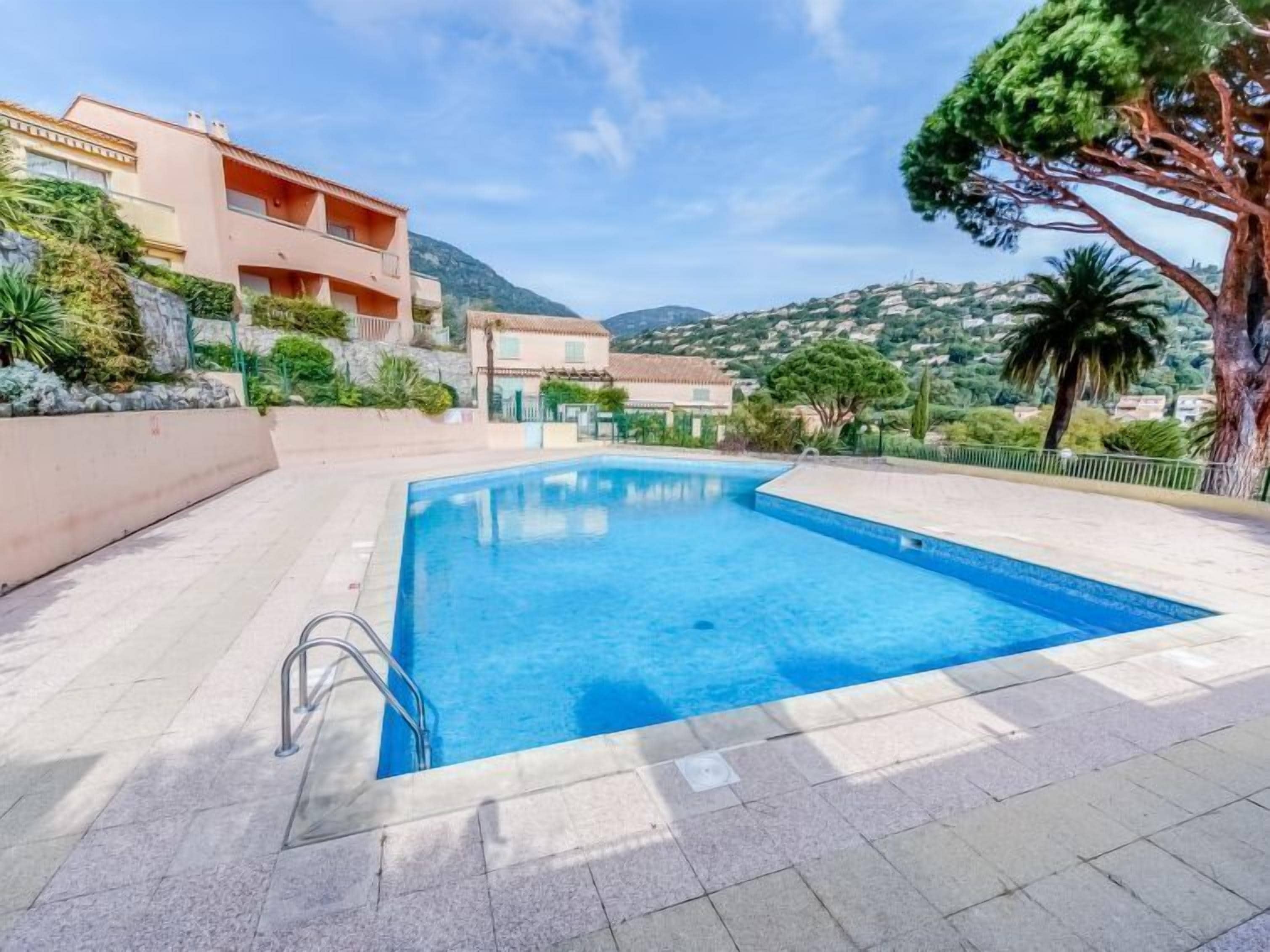 A rectangular swimming pool with a metal ladder on one side, surrounded by a tiled deck.