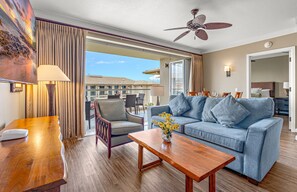 A hotel room with a balcony, a sofa, a wooden table, and a ceiling fan.