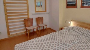 A bedroom with a bed, two wooden chairs, a nightstand with a lamp, a mirror, and two framed pictures on the wall. - Holiday apartment modern and appealing (Bad Mitterndorf)