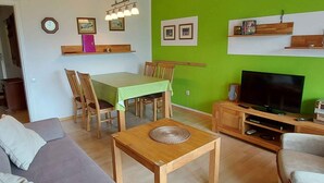 A living room with a green wall, wooden furniture, a TV, and a dining area with a table and chairs. - Holiday apartment modern and appealing (Bad Mitterndorf)