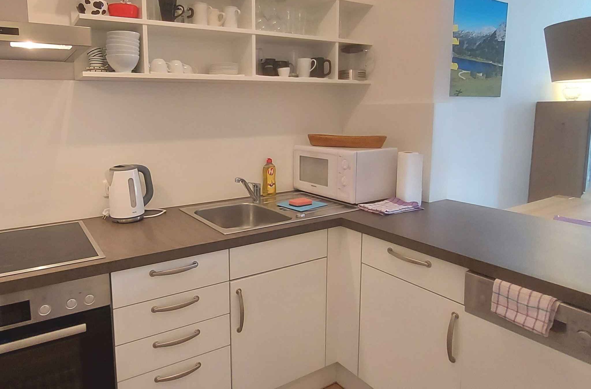 Una cocina moderna con armarios blancos, un lavamanos de acero inoxidable, un microondas y un hervidor.