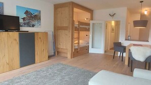 A compact living space with a bunk bed, a television, a desk with a chair, and a white sofa.