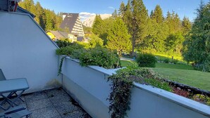 A balcony with a view of a mountain, a garden, and a building with a sloped roof.