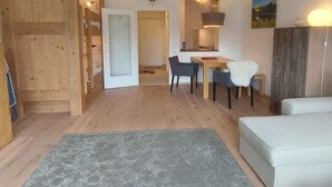 A cozy room with a wooden floor, a dining area with a table and chairs, a sofa, and a large window.