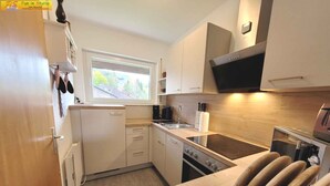 A compact kitchen with white cabinets, a built-in oven, a stovetop, and a window providing natural light.