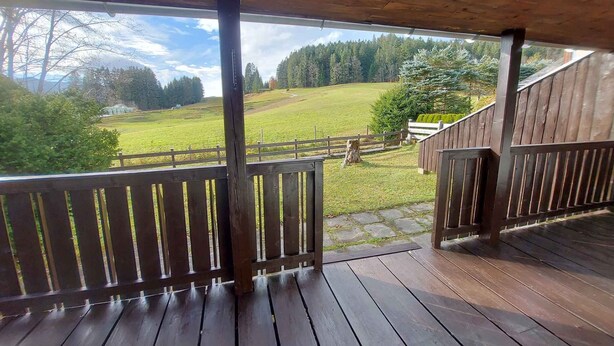A wooden deck with a view of a grassy field and trees.