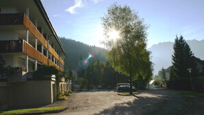 A residential street with a modern building, parked cars, and a tree in the foreground. - Holiday apartment with large balcony (Bad Mitterndorf)