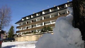 A multi-story building with balconies, a parked car, and snow on the ground. - Holiday apartment with large balcony (Bad Mitterndorf)
