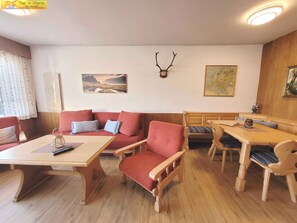 Un salon chaleureux avec un canapé rouge, des chaises en bois, une table en bois et une tête de cerf accrochée au mur.