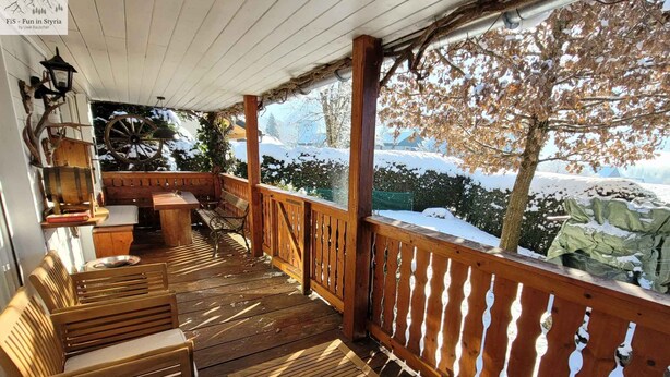 Eine Holzterrasse mit Bänken und einem Tisch, mit Blick auf eine verschneite Landschaft.