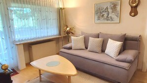 Ein Wohnzimmer mit einer Couch, einem Couchtisch, einem gerahmten Kunstwerk und einer Wanduhr.