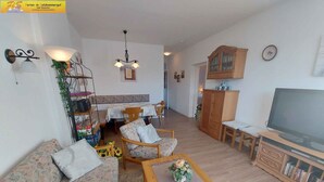 Un saló amb un sofà, cadires, una taula de centre, un televisor, un armari i una zona de menjador amb taula i cadires.