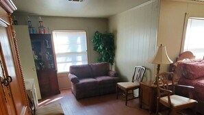 Una sala de estar con piso de madera, un sofá, dos sillones, una lámpara y una planta.