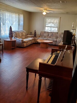 A living room with a piano, a sectional sofa, a coffee table, and a television.