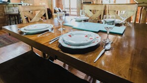 Une table à manger dressée avec des assiettes, des verres et des couverts, entourée de chaises en bois dans un décor rustique.