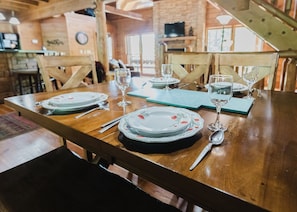 A dining table set with plates, glasses, and cutlery, surrounded by wooden chairs in a rustic interior.