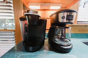 Een kitchenette met een Keurig koffiezetapparaat en een glazen kan op een blauw aanrecht.