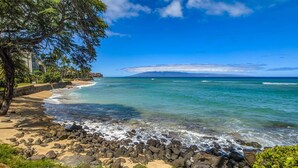 A beach with clear blue water, a rocky shoreline, and a tree-lined path. - Kuleana 613 1 Bdrm 1 Bedroom Condo by RedAwning (Lahaina)