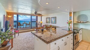 A modern kitchen with a large island, a dining area with a view of the ocean, and a balcony with a view of the sea. - Kaleialoha 209 1 Bedroom Condo by RedAwning (Lahaina)