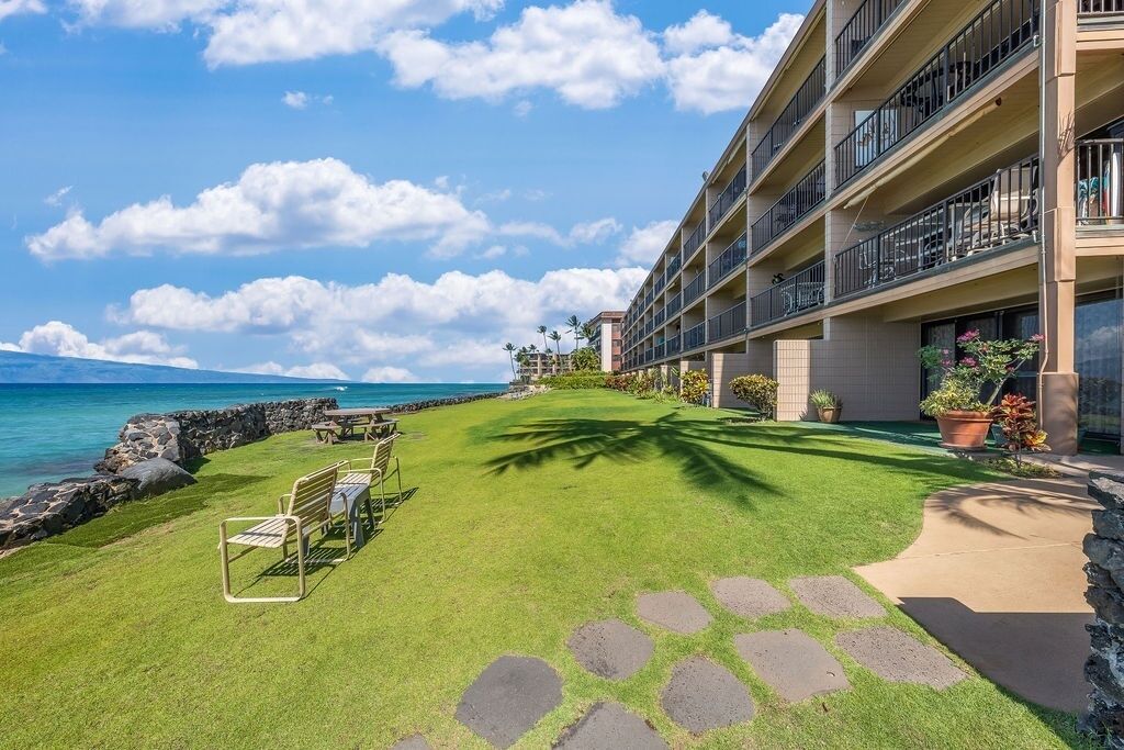 A hotel with a well-maintained lawn, outdoor seating, and a view of the ocean.