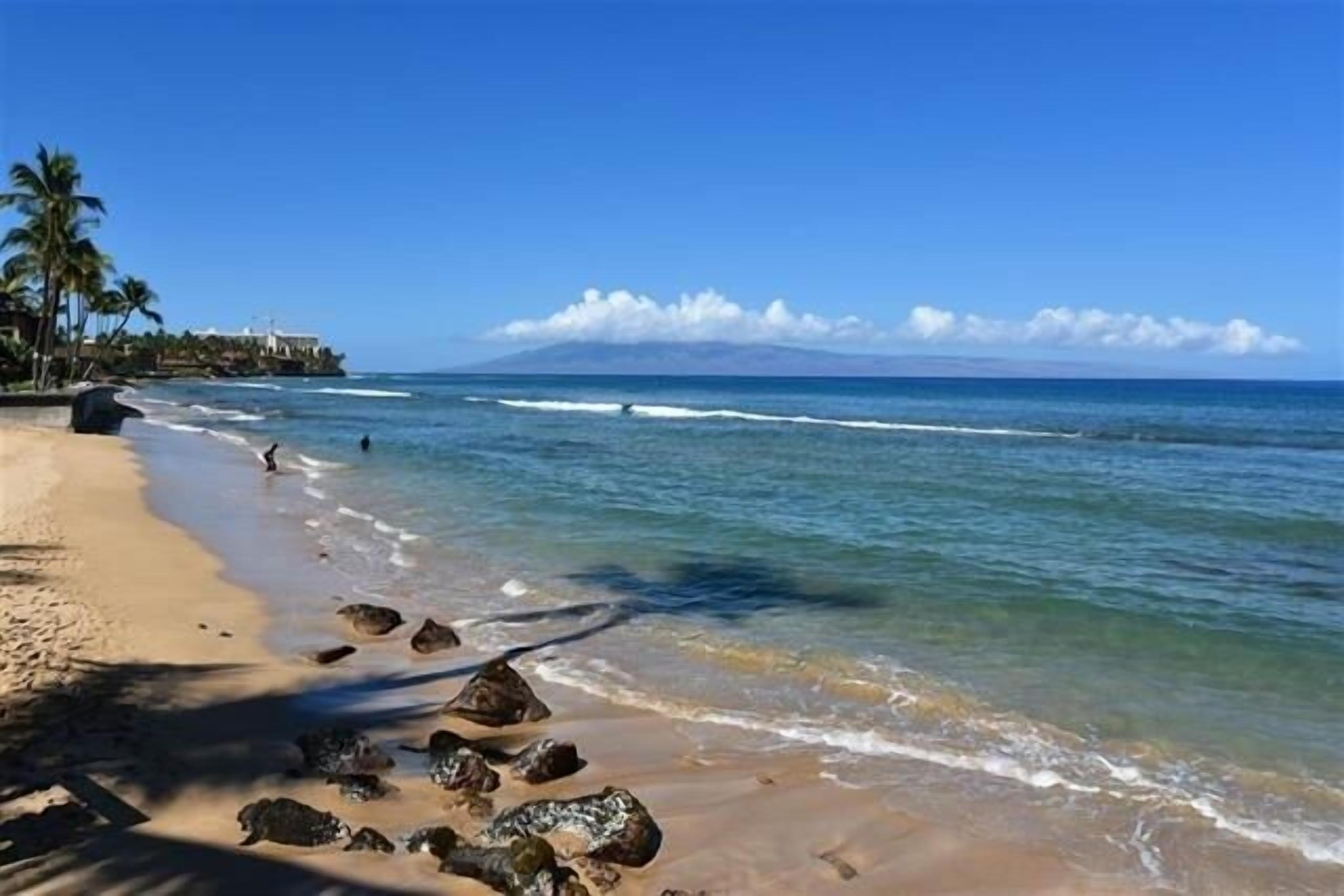 A beach with clear blue water, a sandy shore, and a mountain in the background.