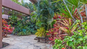 A stone-paved garden with various tropical plants and a bench. - Kaleialoha 209 1 Bedroom Condo by RedAwning (Lahaina)