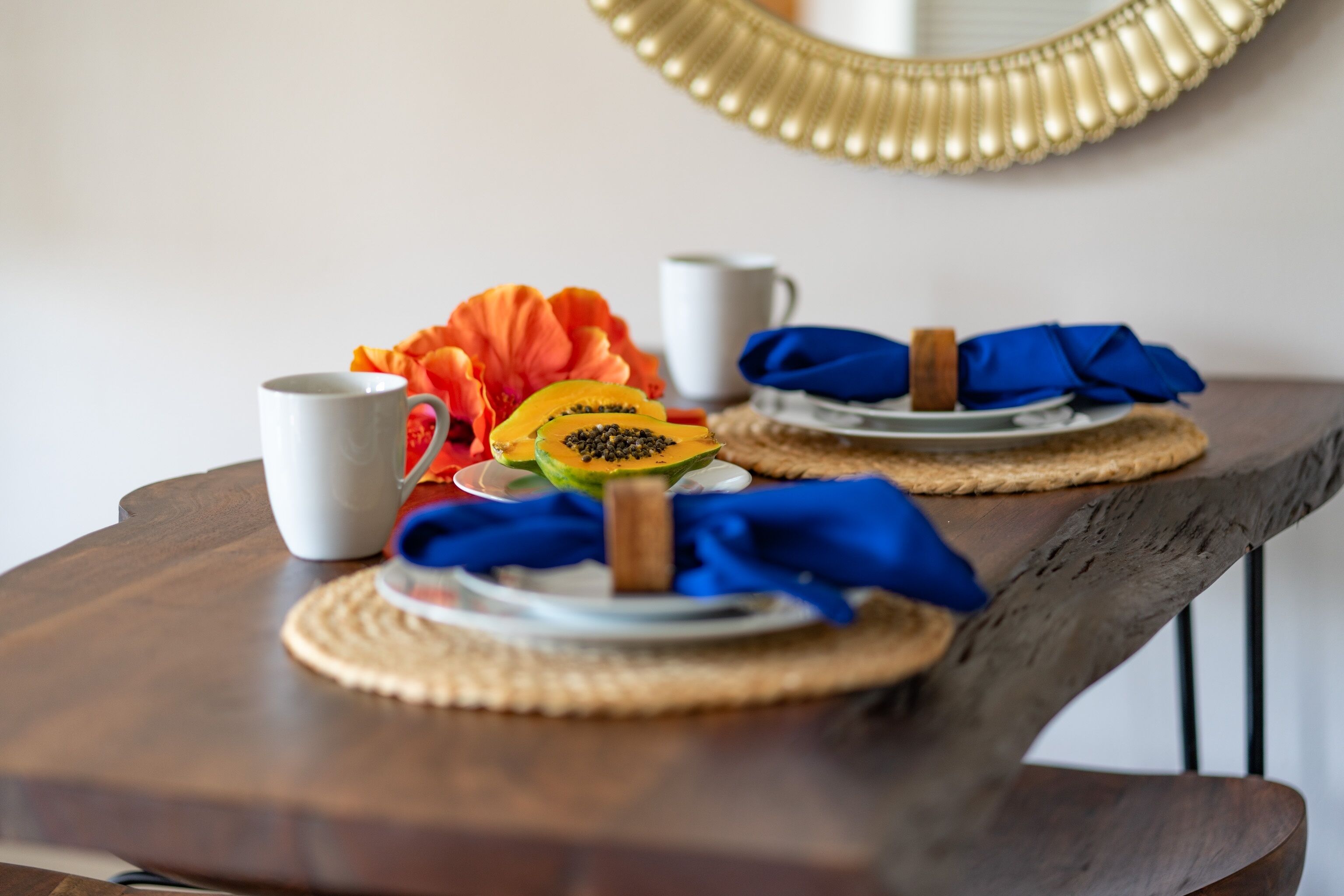 Une table en bois, sur laquelle se trouvent une tasse blanche, une assiette avec des morceaux de fruits et une serviette bleue.