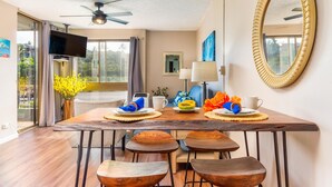 A dining area with a wooden table, four stools, a ceiling fan, and a large mirror on the wall. - Kahana Manor 418 1 Bedroom Condo by RedAwning (Lahaina)