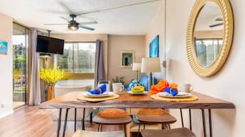 A dining area with a wooden table, four stools, a ceiling fan, and a large mirror on the wall.