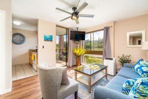 Una sala de estar con sofá, sillón, mesa de centro, televisor y ventilador de techo.