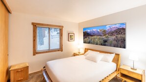 A bedroom with a bed, wooden nightstands, a window with blinds, a framed picture, and a large landscape painting on the wall. - Modern 1 bedroom in Ski Trails by RedAwning (Truckee)