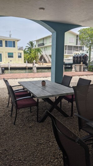 An outdoor patio with a table and chairs, a small potted plant, and a view of a building with a balcony.