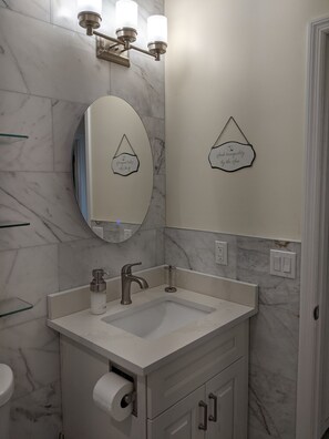 A bathroom with a marble backsplash, a white sink, a modern faucet, a mirror, and two wall-mounted light fixtures.