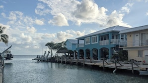 A waterfront property with a dock extending into the water, featuring a blue building with a balcony and a smaller adjacent structure. - 2/2 Ocean, Canal, Dock- Fall Getaway @ Casita Mar! (Marathon)