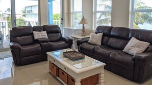 A spacious living room with two leather sofas, a glass coffee table, wicker baskets, and a ceiling fan. - 2/2 Ocean, Canal, Dock- Fall Getaway @ Casita Mar! (Marathon)