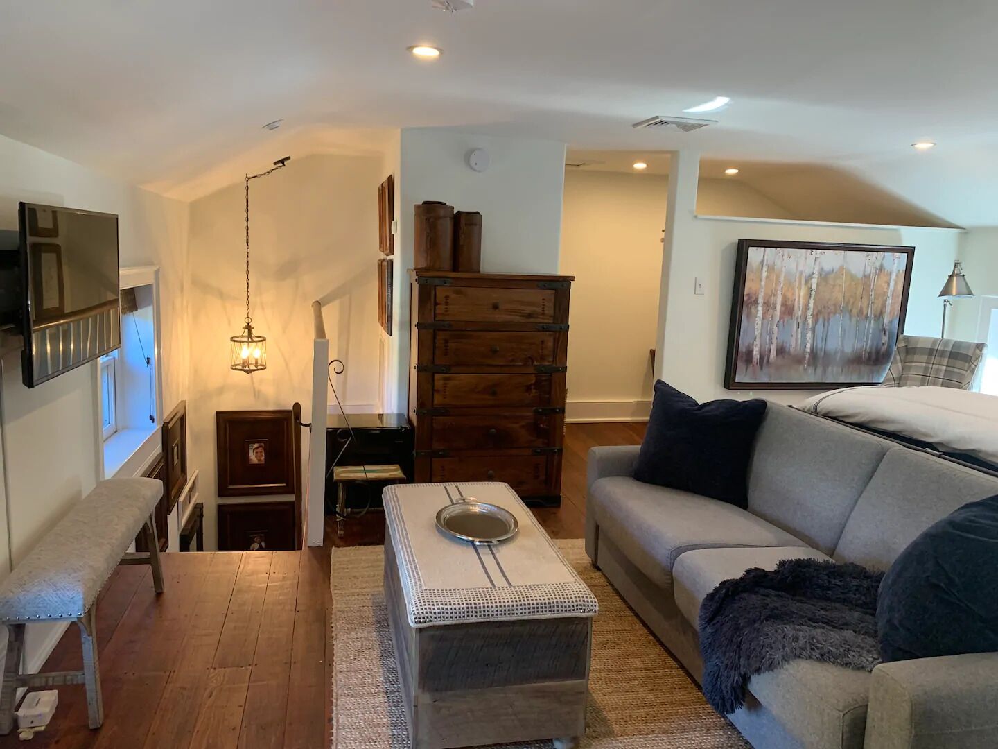 A living room with a wooden floor, a grey sofa, a small table with a glass top, a wooden cabinet, and a painting on the wall.