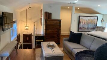 A living room with a wooden floor, a grey sofa, a small table with a glass top, a wooden cabinet, and a painting on the wall.