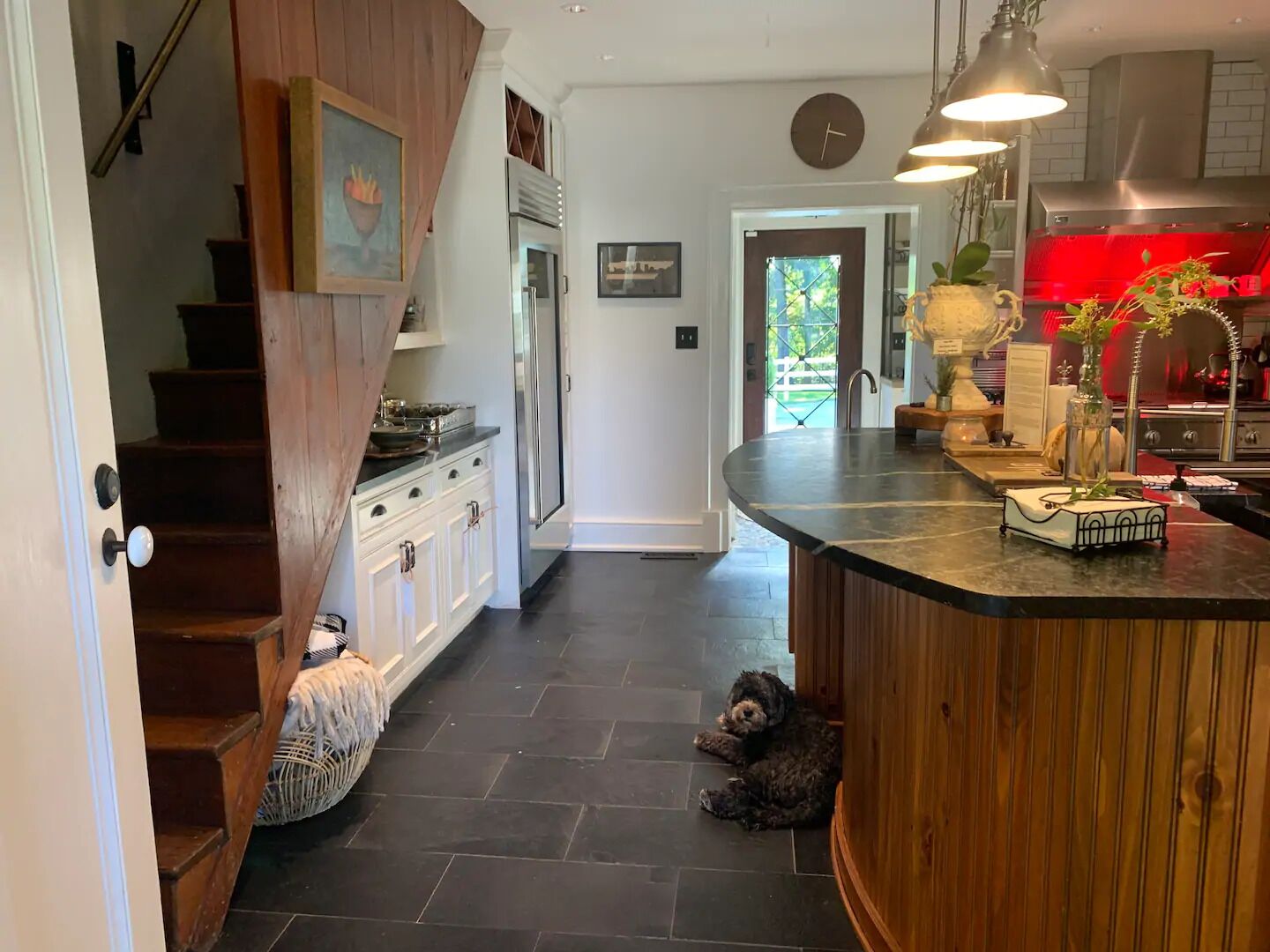 A kitchen with a wooden staircase, a dog resting on the floor, and a red-lit stove area.