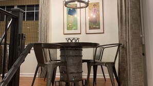 Uma sala de jantar com uma mesa redonda, cadeiras, um candelabro e duas quadros nas paredes.