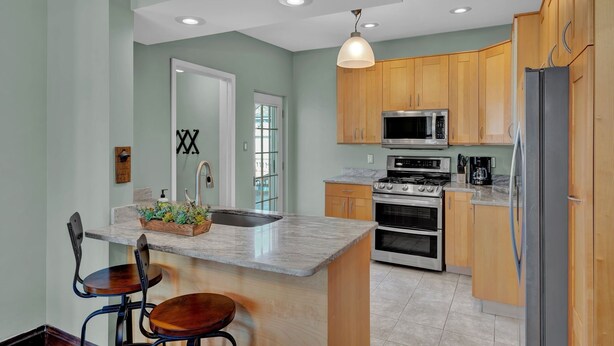 A modern kitchen with wooden cabinets, stainless steel appliances, and a central island with seating. - Oakley Square 3br Charmer - Total Walkability 3 Bedroom Home by RedAwning (Cincinnati)