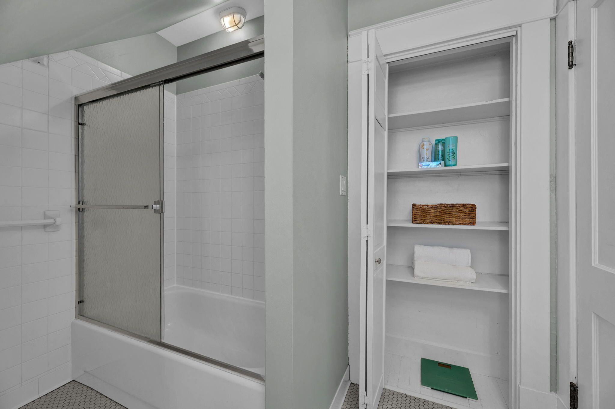 A bathroom with a glass-enclosed shower, a white bathtub, and a built-in shelf with toiletries.