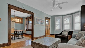 A spacious living room with hardwood floors, a wooden coffee table, a sofa, and a dining area with a table and chairs. - Oakley Square 3br Charmer - Total Walkability 3 Bedroom Home by RedAwning (Cincinnati)