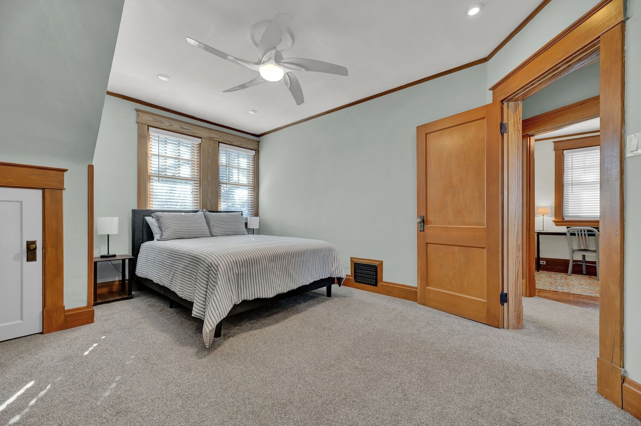 A bedroom with a large bed, a ceiling fan, and a door leading to another room.